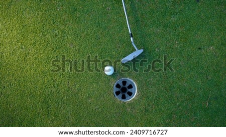 Selective focus. white golf ball in hole on green grass good for background with sunlight. Putter and golf ball beside the golf hole.                               