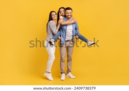 Happy European Family Of Three Having Fun Together Over Yellow Background, Cheerful Young Parents And Their Teen Daughter Laughing And Smiling At Camera, Girl Piggybacking Dad, Copy Space