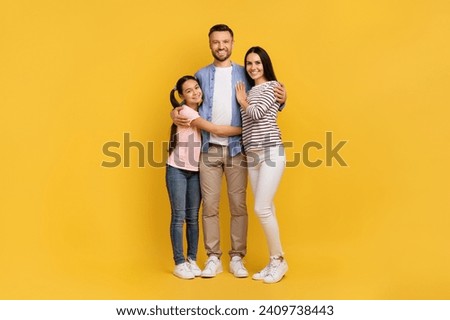 Family Portrait. Happy Young Parents And Their Teen Daughter Embracing Over Yellow Background, Full Length Shot Of Cheerful Mother, Father And Teenage Child Hugging Together In Studio, Copy Space