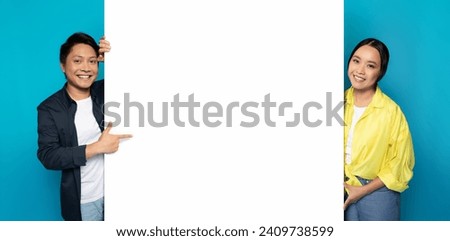 Asian millennial man and woman happily pointing at a vast blank white space, ideal for advertisements or custom content, set against a half turquoise, half white background