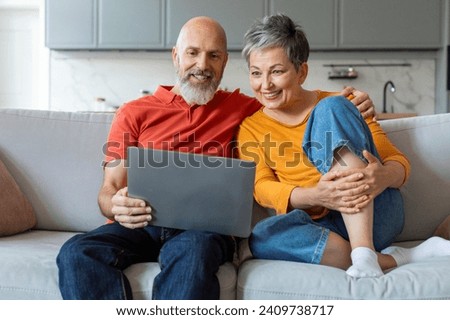 Happy Senior Couple Watching Movie On Laptop At Home, Smiling Elderly Spouses Relaxing On Couch With Computer, Older Man And Woman Resting In Living Room Interior, Enjoying Domestic Leisure