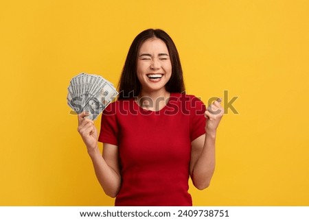 Emotional Asian Woman Holding Money Cash Grimacing And Gesturing, Standing Over Yellow Background. Lady Posing With Dollar Banknotes. Financial Success, Profit And Currency Concept