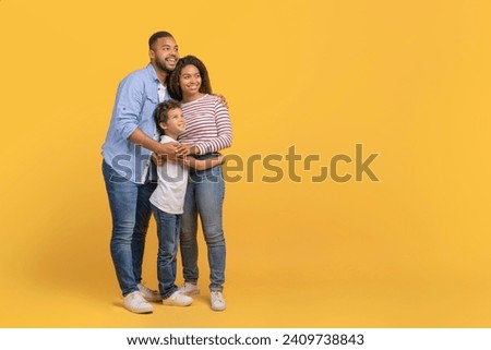 Happy African American Parents And Son Embracing And Looking Aside At Copy Space, Cheerful Loving Black Family With Preteen Male Child Posing Together On Yellow Studio Background, Full Length