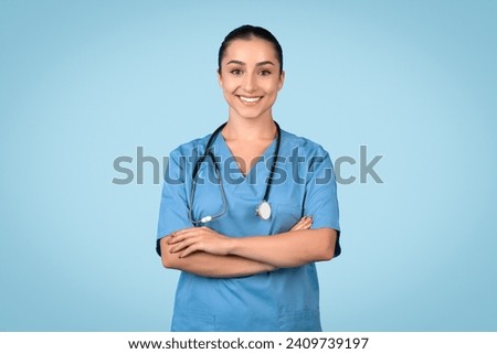Confident and smiling female nurse in blue scrubs, arms crossed, with stethoscope around her neck, representing healthcare professionalism, blue background