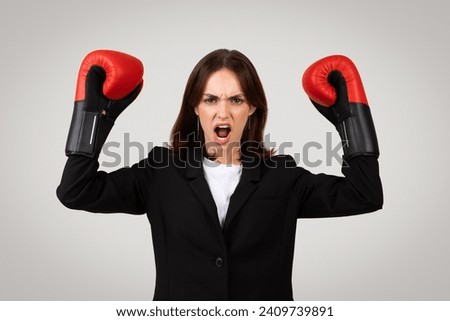 Confident strong young European lady winner in suit, boxing gloves rise fists, scream, enjoy win, isolated on gray studio background. Business work and fight, power lifestyle