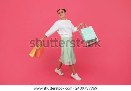 Seasonal Sales Concept. Smiling Asian Woman Walking With Shopping Bags Over Pink Background In Studio, Happy Korean Lady Wearing Stylish Eyeglasses Enjoying Making Purchases, Full Length, Copy Space Royalty-Free Stock Photo #2409739969