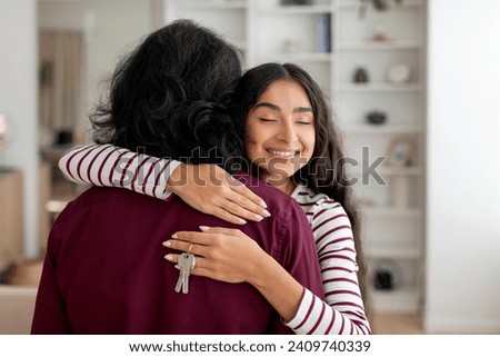 Young beautiful indian lady hugging her husband and holding house key in their new apartment, copy space. Happy millennial couple embracing indoors on moving day. Relocation concept
