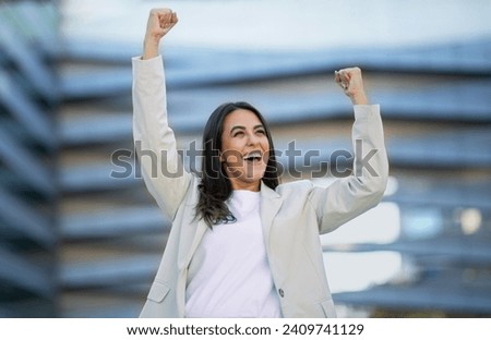 Business Success, Career Achievement. Joyful Arabic Business Lady Shaking Arms In Yes Gesture, Standing Outside In Urban Area, Near Modern Office Center Building. Triumph Celebration Concept Royalty-Free Stock Photo #2409741129