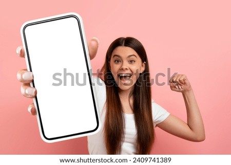 Online offer. Overjoyed teen girl celebrating success, shake fists and showing big phone with white blank screen at camera, emotionally reacting to win while standing over pink background, copy space