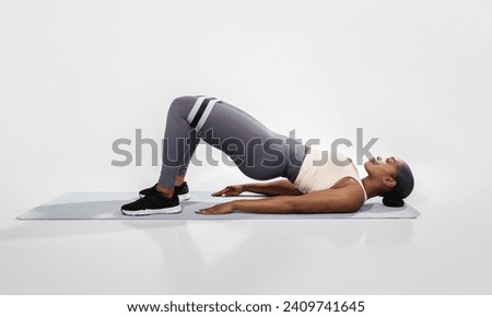 Fitness Concept. Sporty Young African American Woman Doing Glute Bridge Exercise With Resistance Loop, Athletic Lady Training Buttocks And Legs Muscles, Having Workout Over White Studio Background Royalty-Free Stock Photo #2409741645