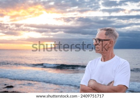 Senior mature man at the sea beach at sunset light looking the horizon over sea admiring the orange sunray and cloudy sky, handsome man enjoys a relaxed retirement lifestyle Royalty-Free Stock Photo #2409751717