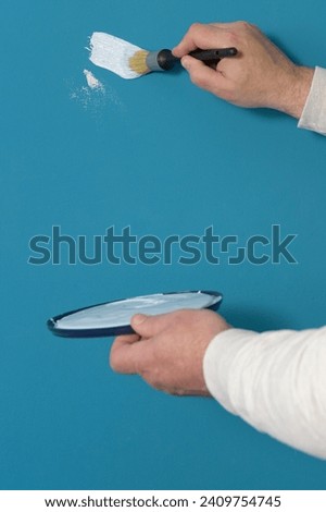 Test of color and quality of paint. a brush in a man's hand and smears of light blue paint on a dark blue wall