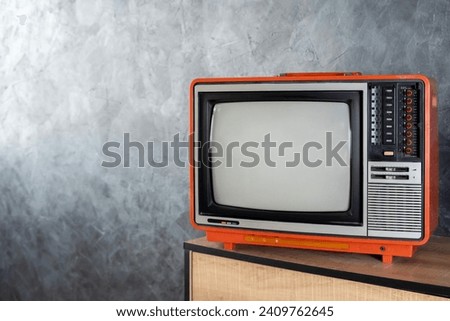 Old television concept. A vintage television set sits on a dresser in a bedroom. A retro television with a blank screen sits in a room.  An old, orange television set is turned off.