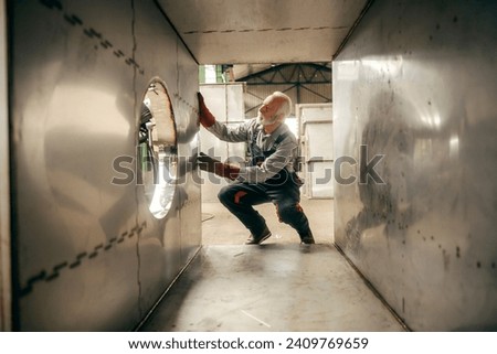 A senior metallurgy and heavy industry worker is making metal container in factory. Royalty-Free Stock Photo #2409769659