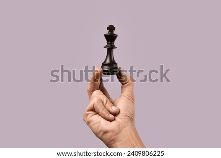 Male hand holding king chess figure on purple background. Royalty-Free Stock Photo #2409806225