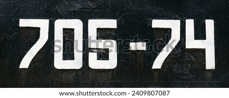 Weathered numbers 7, 0; 5, 4, seven, zerro, five, four, or 70574 painted white on a piece of black metal. Abstarct numeral background for design. Royalty-Free Stock Photo #2409807087