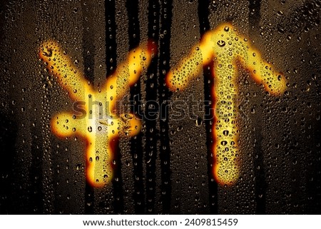 Blurred glowing Chinese Yuan sign with arrow up made from light bulbs.The symbol of the national currency behind a rain-wet window with water drops in the night.Sign of economic rise.