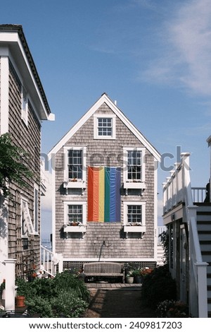 Nestled in a charming coastal town, this quaint house adorned with a pride flag symbolizes inclusive and diversity. The welcoming facade, complete with blooming flowers and classic white picket fence