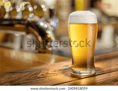 Glass of chilled beer on wooden bar table top and blurred bar interior at the background.