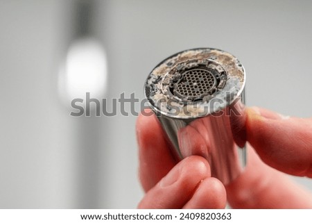 A plumber is holding a chrome faucet aerator with lime scale in kitchen room  Royalty-Free Stock Photo #2409820363