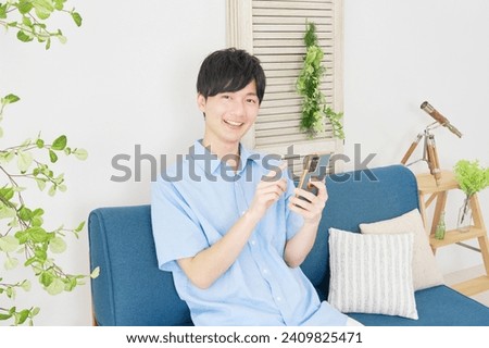 Asian man using the smartphone at the living room, looking at camera