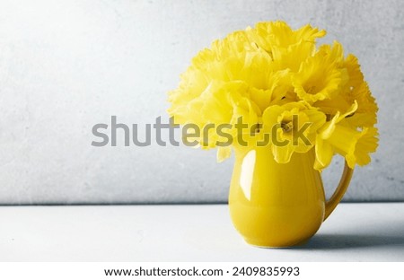 Bouquet of yellow daffodils in a yellow jug on table top, home decor, interior, copy space