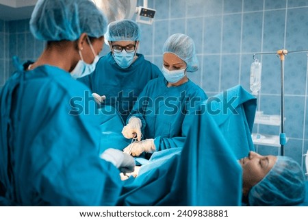 Team of experienced surgeons wearing wearing protection, surgical caps and masks working together in a operation room. Medical staff of professional surgeons performing surgery on a patient.