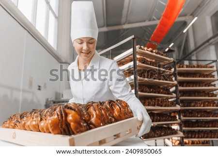 Worker woman baker in chef uniform rack with poppy seeds. Different types of artisan craft bread in bakery factory. Industry food plant.