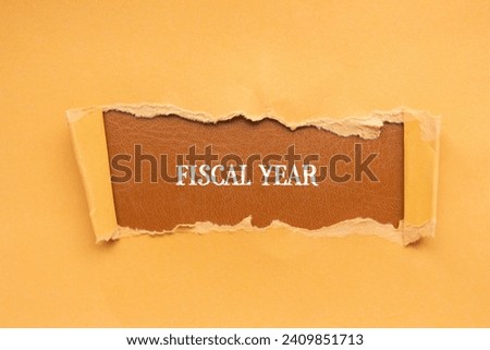 Fiscal year lettering on ripped orange paper with brown background. Conceptual business photo. Top view, copy space for text.