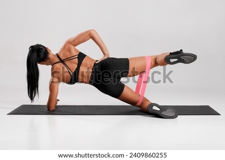 Fitness woman doing clamshell exercise for glutes with resistance band on gray background. Athletic girl working out Royalty-Free Stock Photo #2409860255
