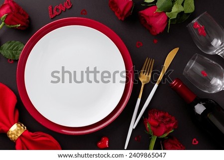 Memorable Valentine's Day dining event. Top view photo of plates, cutlery, hearts, red roses, wineglasses, presents, red napkin, wine bottle, candle on black background with advert zone Royalty-Free Stock Photo #2409865047