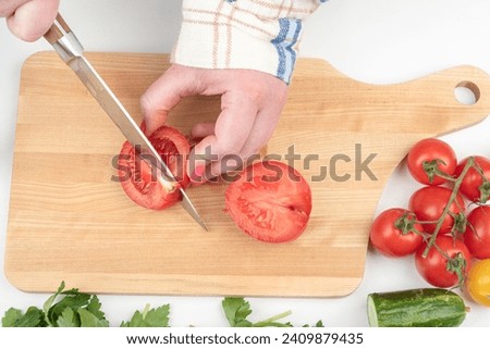 Cutting with a knife will not edible part of the tomato on the cutting board. Home cooking. Royalty-Free Stock Photo #2409879435