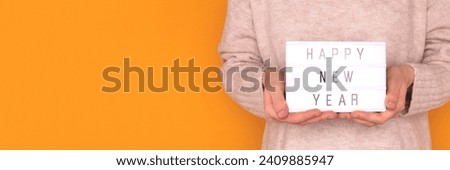 Banner with quote Happy New Year. Woman hold in hands lightbox with letters in front of yellow background. Place for text.