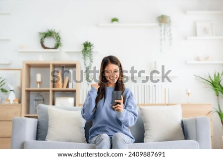 Happy young asian woman relax on comfortable couch at home texting messaging on smartphone, smiling girl use cellphone, chatting online message, shopping online from home Royalty-Free Stock Photo #2409887691