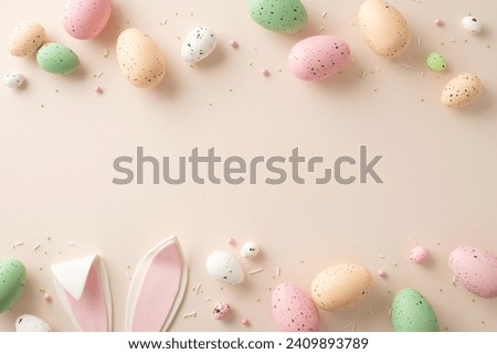 A festive Easter scene unfolds in this top-view snapshot. Vibrant eggs, endearing bunny ears and sprinkles decorate a pastel beige surface with an open area for your text or advertisement Royalty-Free Stock Photo #2409893789