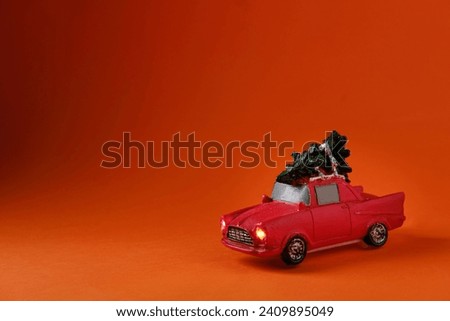 A small red toy with a green Christmas tree on the roof, on an orange background, side view