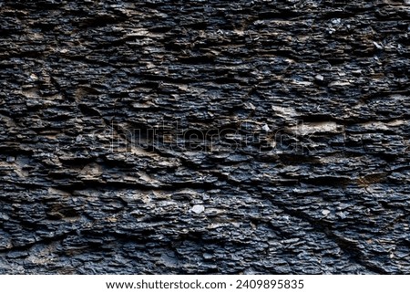 Slate rock background with dark stone layers, cracks caused by erosion. Wet rough surface near a waterfall in Germany. Fine-grained, foliated geologic formation in shades of grey and brown. Royalty-Free Stock Photo #2409895835
