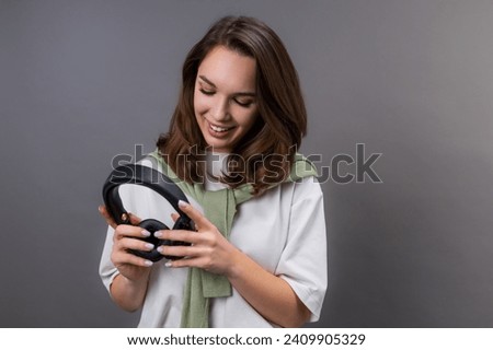 A young woman puts on headphones before listening to music on a gray background in the studio. Enjoyment of music