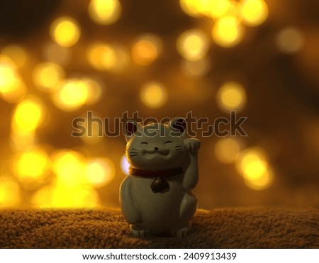 Maneki-Neko Japanese figurine with golden bokeh background (lucky cat, calling cat, waving cat, beckoning cat) Royalty-Free Stock Photo #2409913439