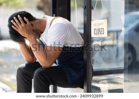 Young man running a small start-up business sits at the entrance looking absent-minded. Entrepreneurs starting small startups are stressed out and forced to close shop due to the economic crisis. Royalty-Free Stock Photo #2409932899