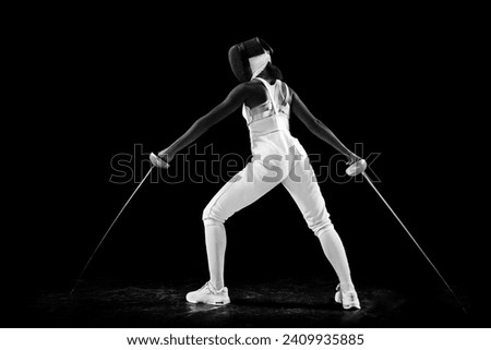 Dual-blade mastery portrait of female fencing maestro, confidently posing with two swords against black studio background. Artistry and precision of sport Concept of professional sport, championship.