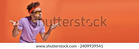 african american man in eyeglasses pouting lips and gesturing on orange background, banner