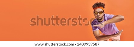 cool african american sportsman in gym attire and sunglasses gesturing on orange background, banner