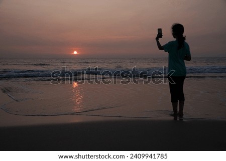 Young girl taking sunset picture on mobile on Kondivali beach, Raigad, Maharashtra, India, Asia.