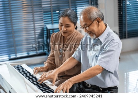Asian senior elderly couple play piano together in living room at home. Loving older mature grandmother and grandfather feel happy and relax while spend leisure time learning music classroom at home.