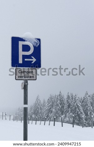 Parking lot traffic sign, but camping is prohibited (German: "Campen verboten" means camping prohibited). Snow-covered winter landscape with wooden pasture fence.
