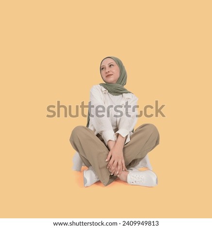 Shy girl looking aside, full body portrait of young muslim shy girl looking aside. Wear hijab, sit floor legs crossed. Dreaming imagining idea. Feeling embarrassed. Light orange studio background. Royalty-Free Stock Photo #2409949813