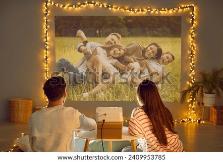 Projection family pictures on wall, using video projector, happy people in love sitting close enjoy romantic moment. Home theater evening movie emotion, loving male, female pair celebrate holiday 