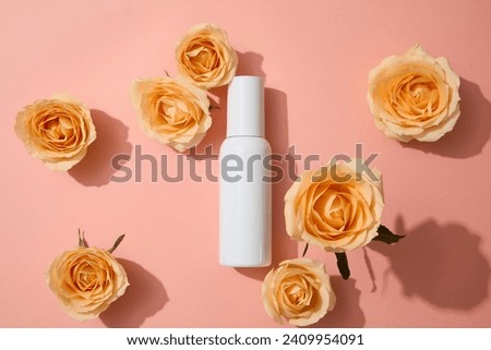 Top view of an unlabeled bottle on pink background with fresh roses. Rose extract Vitamin C shields skin from UV rays, preventing aging. Cosmetic concept. Royalty-Free Stock Photo #2409954091