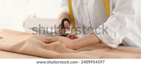 Dressmaker cutting fabric with scissors at table in workshop, closeup. Banner design Royalty-Free Stock Photo #2409954597
